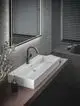 Waschbecken mit schmalem, rechteckigem Design auf Holzablage, kombiniert mit einer Wascharmatur von Ideal Standard in mattem Schwarz und einem beleuchteten Spiegel über dem Becken.